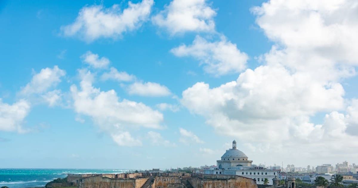 A scenic view of San Juan, featuring El Capitolio and historic fortifications under a bright blue sky.