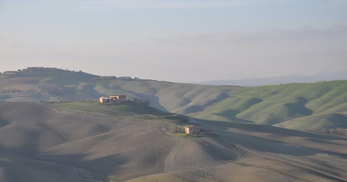Beautiful rolling hills and farmhouses in Asciano, Tuscany captured during daylight.