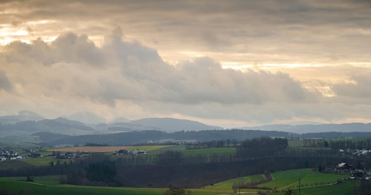 Breathtaking view of rolling hills and fields under a dramatic sunset sky.
