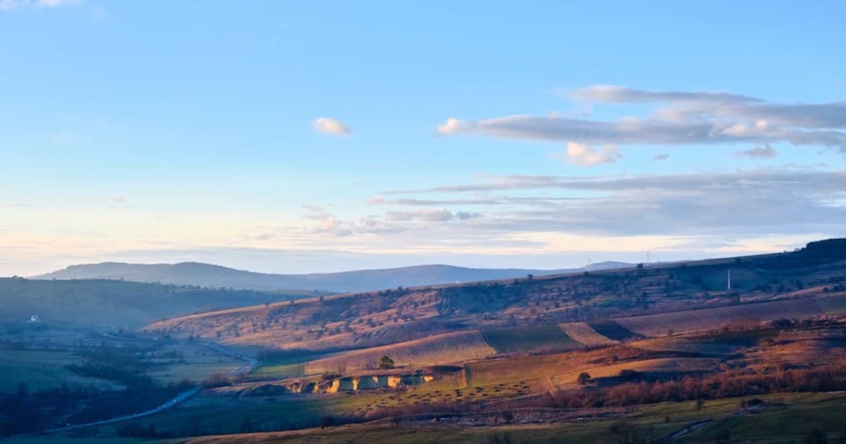 Beautiful landscape of rolling hills with soft sunset lighting and scattered clouds.