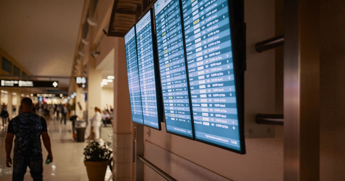 Airport terminal with digital flight information boards showing arrivals and departures.