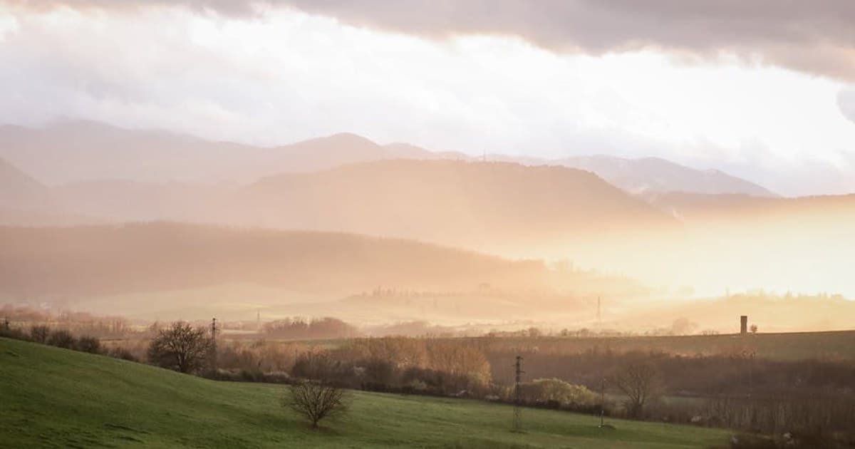 Peaceful sunlit landscape view over Anagni's rolling hills with misty mountains.