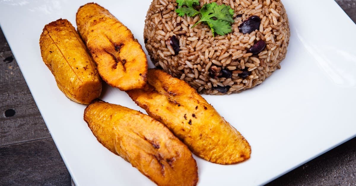 A savory plate of rice and beans with fried plantains on a white plate, garnished with parsley.